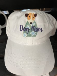 White cap with an illustration of a dog and the words "Dog Mom" printed on the front.
