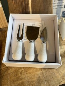 A boxed set of three cheese knives with white handles displayed on a wooden surface.