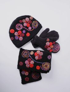 A black knit hat, mittens, and scarf set decorated with colorful embroidered spiral and circular patterns.