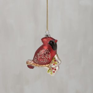 Red cardinal bird ornament with glitter details, hanging by a gold string against a neutral background.