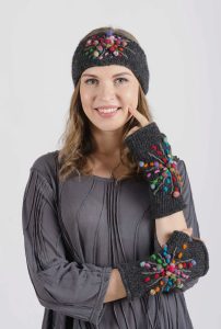 Woman wearing a grey headband and fingerless gloves with colorful pom-poms, dressed in a grey pleated top.