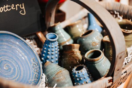 A basket filled with various small blue and green ceramic pots and vases, next to a blue glazed plate.