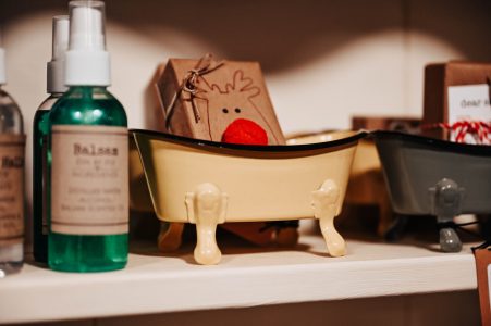 A small yellow bathtub-shaped container on a shelf next to bottles and a reindeer-themed box with a red nose.