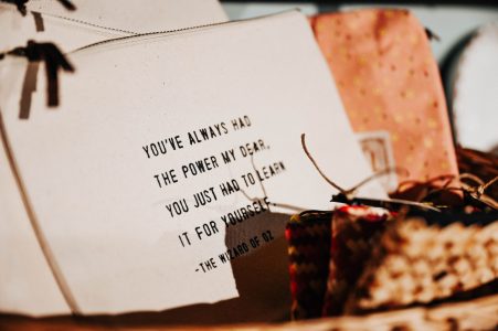 A fabric pouch with black text quoting The Wizard of Oz, surrounded by other patterned pouches and woven items.