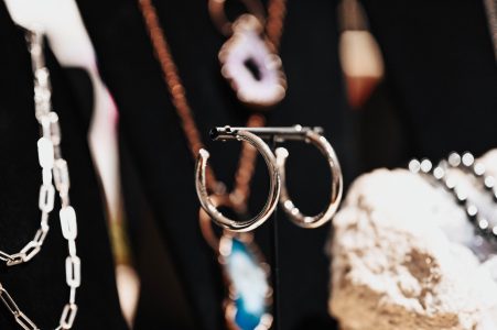 Silver hoop earrings displayed on a stand, with necklaces and a decorative stone in the blurred background.