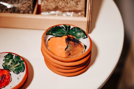 A stack of small ceramic plates with hand-painted fruit designs sits on a white table next to a wooden box.