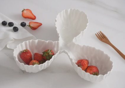 A three-section white ceramic dish holds strawberries, with blueberries and a wooden fork nearby on a white surface.