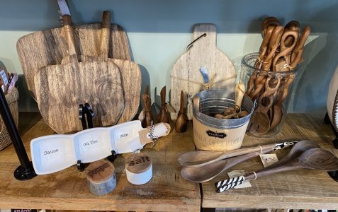 Display of wooden kitchen utensils, cutting boards, a sauce dish set, and salt and pepper containers on a wooden table.