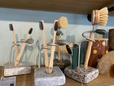 Three stone-based stands hold bamboo toothbrushes, cleaning brushes, and sponges arranged in an upright display on a shelf.