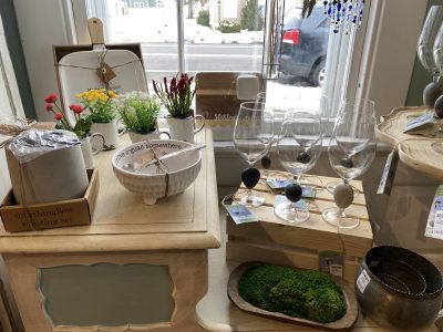 A display of home decor items, including wine glasses, fake plants, a moss dish, and a marshmallow roasting set.