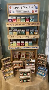 Wooden display shelf with assorted Spicewalla spice boxes and sets, labeled “Superb Spices and Seasonings.”.