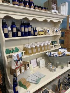 A display shelf holds blue bottles, pump soaps, bar soaps, sachets, tins, and spa products in a shop.
