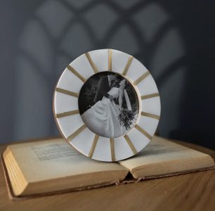 Round photo frame with gold accents displaying a wedding portrait, placed on an open book against a gray background.