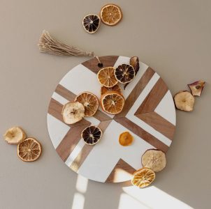 A round wooden and white board with geometric patterns and assorted dried citrus slices arranged on top.