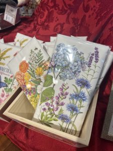 Greeting cards with colorful botanical illustrations displayed upright in a wooden box on a red tablecloth.