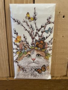Illustration of a cat with branches, leaves, and butterflies on its head, against a wooden background.