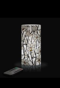 A floral-patterned lamp emits soft light, with a remote control placed nearby on a black surface.