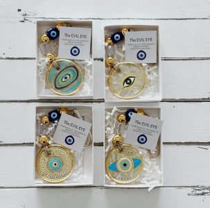 Four decorative evil eye keychains in boxes with descriptive cards and blue glass beads on a white wooden surface.