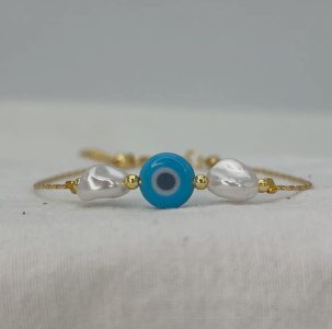 A gold bracelet with a blue evil eye bead in the center, flanked by two pearl-like beads and small gold accents.