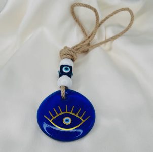 A blue evil eye charm with beads and rope, displayed on a white fabric background.