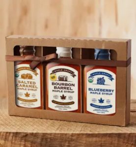 A cardboard box containing three bottles of maple syrup: salted caramel, bourbon barrel, and blueberry flavors.