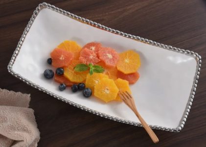 Sliced citrus fruits and blueberries arranged on a rectangular white plate with a small wooden fork and mint garnish.