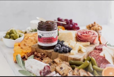 A charcuterie board with cheese, meats, nuts, fruit, olives, and a jar of Terrapin Ridge Farms hot pepper bacon jam.