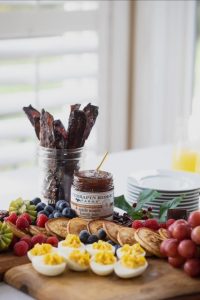 A breakfast platter with deviled eggs, pancakes, fruit, bacon in a jar, and apple maple bacon jam in the center.