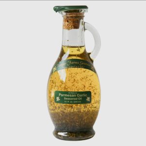 A glass bottle of Flavgar Farms Gourmet Parmesan Garlic seasoned oil with herbs visible inside.