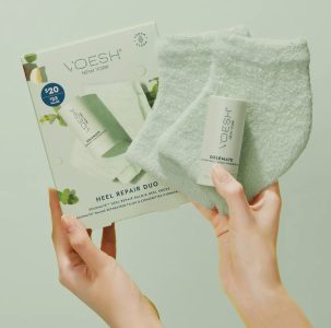 A person holds a box of Voesh Heel Repair Duo, showing matching soft socks and a Solemate foot balm stick.