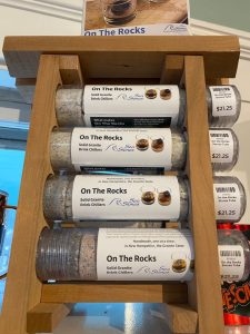 Three tubes labeled "On The Rocks" solid granite drink chillers displayed on a wooden rack, each priced at $21.25.