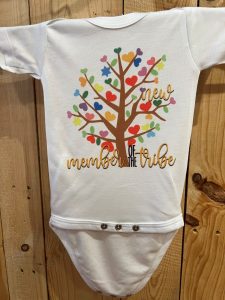 White baby onesie with a colorful heart tree graphic and the text "new member of the tribe" printed on it.