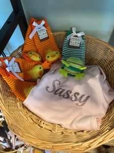 A basket with a pink "Sassy" shirt, two pairs of striped animal baby socks—one with ducks, one with frogs.