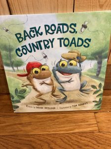 Children’s book titled "Back Roads, Country Toads" shows two cartoon toads wearing hats on the cover.