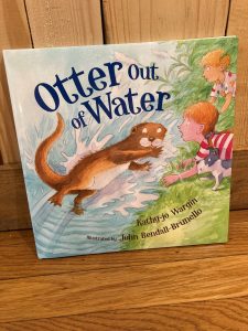 Children’s book titled "Otter Out of Water" by Kathy-jo Wargin, illustrated by John Bendall-Brunello, on a wooden surface.