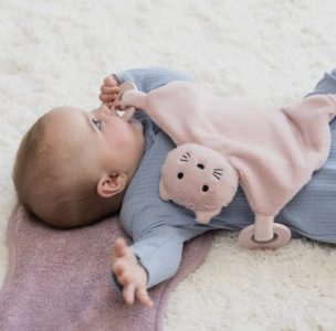Baby lying on a soft surface holding a pink plush animal comforter with a pacifier attached.
