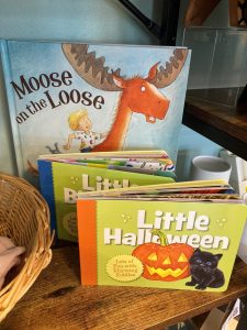 Children’s books titled "Moose on the Loose" and "Little Halloween" displayed on a wooden shelf.